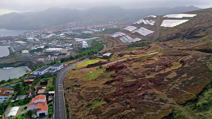 Cloudy panorama coastal city on green slopes. Solar panels covering hillside