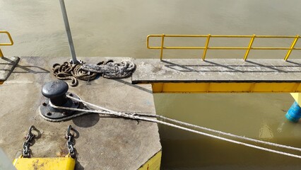 Fototapeta premium Yellow Dock Pier with Ropes and Bollard by the River Edge