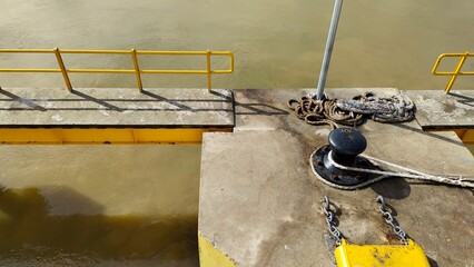 Obraz premium Yellow Dock Pier with Ropes and Bollard by the River Edge