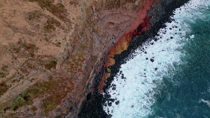 Top foamy waves splashing on volcanic dark stones shoreline. Stormy sea water 