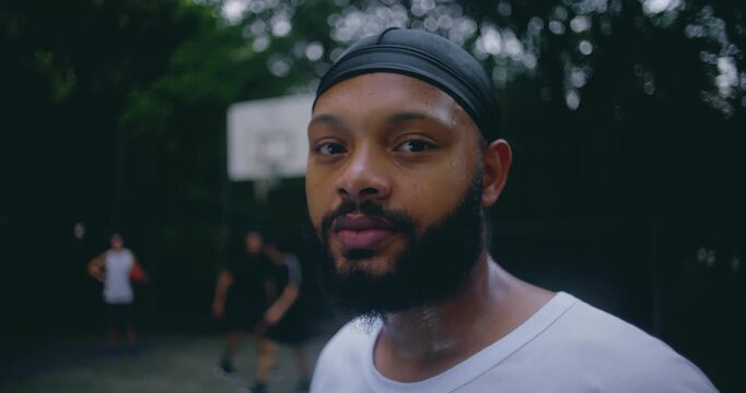 Portrait of basketball player of African descent in white shirt with durag, standing on outdoor court after intense game, sweat showing athletic effort