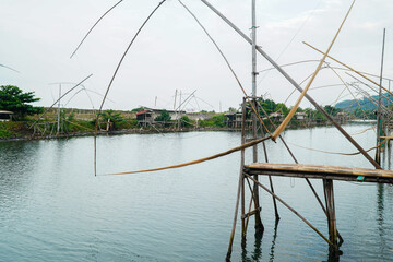 Fototapeta premium A tranquil scene featuring traditional fishing structures standing tall in calm water, embodying a serene and timeless fishing tradition, with the still water mirroring the overcast sky.