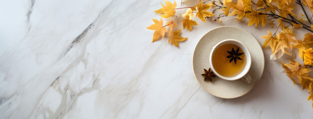 Cup of warm tea with star anise on white marble background. Autumn season beverage with fall leave for hot drink concept. Blank space.