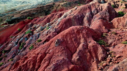 Aerial eroded red cliffs with rock layers stones scattered across slopes. 