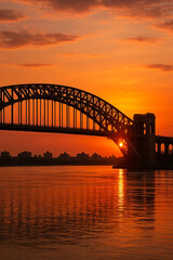 Obraz premium Steel arch bridge over river at sunset with city skyline in the background