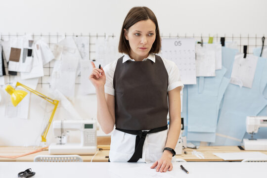Inspired fashion designer at work. Young woman working on new collection of clothes, standing by table and drawing garment sketches