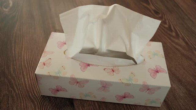 A box of tissues with butterflies on it sits on a wooden floor