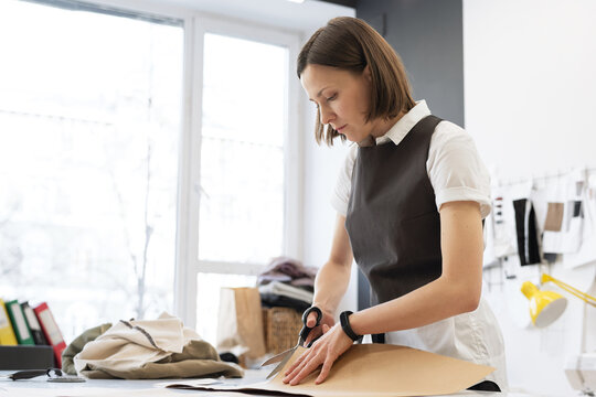 Woman working in atelier. Young concentrated female tailor cutting sewing patterns for clothing out of cardboard