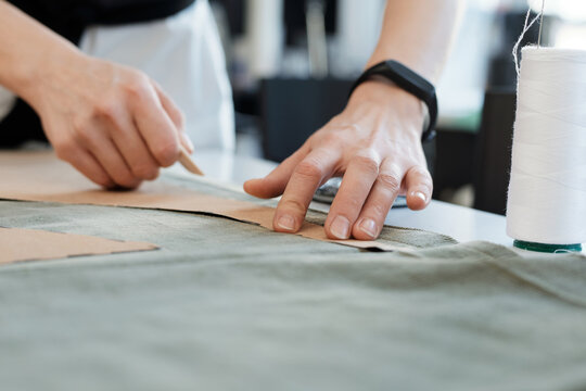Tailor working with templates. Close-up view of female hands outlining sewing patterns on garment fabric with chalk