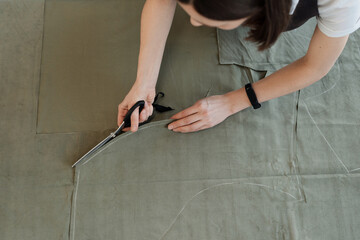 High angle view of unrecognizable female tailor cutting pattern pieces out of fabric outside the tracing lines