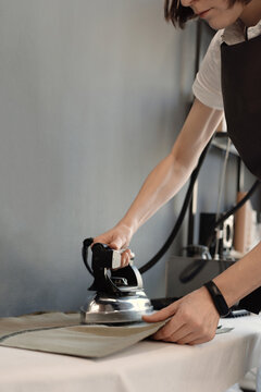 Unrecognizable professional female tailor ironing finished garment in atelier