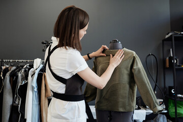 Professional female custom tailor dressing mannequin in unfinished garment in atelier