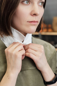 Portrait of young thoughtful Caucasian woman trying on new garment, buttoning up and looking into the distance