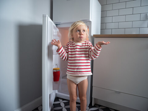 Little girl looking into an empty fridge and spreading her arms in confusion