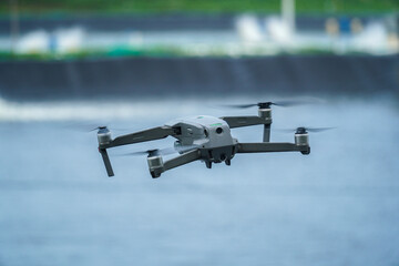 Aerial inspection using a modern drone. Gray drone hovers above water, with propellers spinning,...