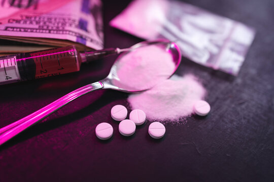 Neon-lit scene with syringe, white pills, powder and money banknotes on dark background, concept of drug addiction, substance abuse and nightlife risks