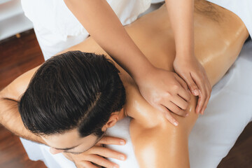 Caucasian man customer enjoying relaxing anti-stress spa massage and pampering with beauty skin recreation leisure in day light ambient salon spa at luxury resort or hotel. Quiescent