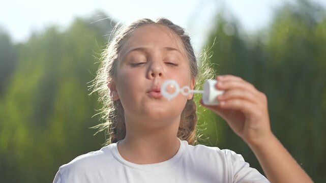 Girl play soap bubbles in park. Happy girl blowing soap bubbles on sunny day. Joyful playtime as girl enjoys soap bubbles in park. Carefree childhood moments with soap bubbles. Girl fun play in nature