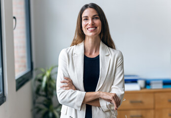 Beautiful businesswoman taking a break while looking at camera next to the window at the office.