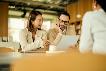 Asian Woman and Man Collaborate Over Document in Modern Office Cafe Setting