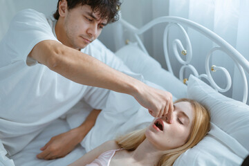 Fototapeta premium A young man is trying to stop his wife from snoring because she snores very loudly.
