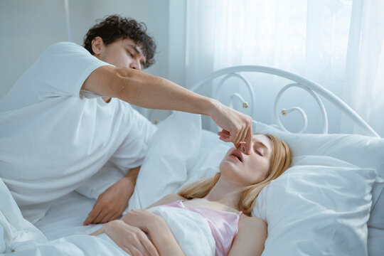 A young man is trying to stop his wife from snoring because she snores very loudly.