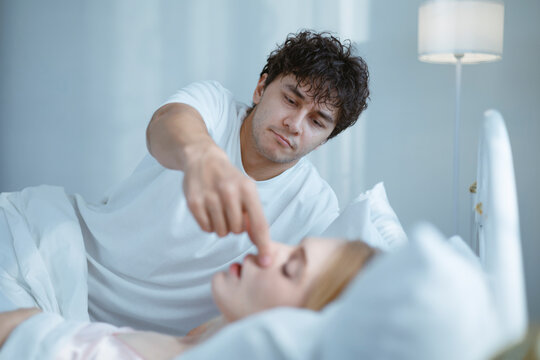 A young man is trying to stop his wife from snoring because she snores very loudly.