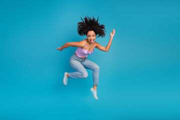 Young woman jumps with joy in blue studio background showcasing fashion style energy happiness and confident self expression for lifestyle advertising