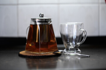 brewing tea in a glass teapot and next to it is a glass mug with herbs and crumbly tea scattered on the table