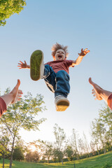 Amazed funny boy laughing while flies into the arms of his dad who tosses him high during a family fun time in a park. POV view