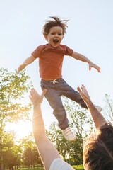 A dad throws his cheerful little boy up in the air at a park during sunset, sharing joyful playtime and father-son bonding on a summer evening. 