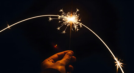 Close-up of a hand holding a lit sparkler in the dark. Focus on light trail and holiday cheer.