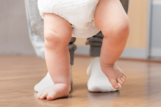 A baby learns to walk with his dad. Close-up of his legs.