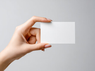 Obraz premium Female hand holding blank white business card on neutral gray background with perfect manicure for branding and marketing mockup concepts