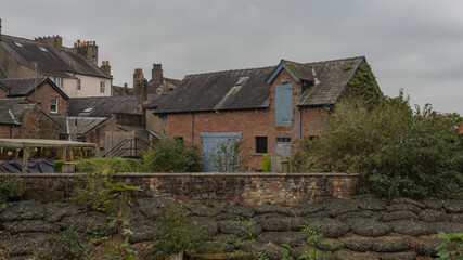 Fototapeta premium An old stone barn with a slate roof and peeling blue wooden doors sits behind a low stone wall in a traditional English village. 