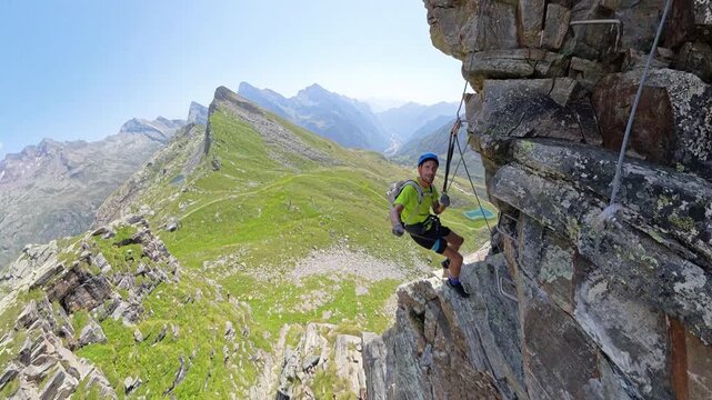 Aerial view of a solo climber taking a break while hanging from ropes with the Alps stretching below. Via Ferrata Cimalegna, Alagna Valsesia, Italy