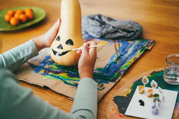 Female kid painting a pumpkin for an halloween party fest - Holidays, education without technology and art concept - Main focus on right hand