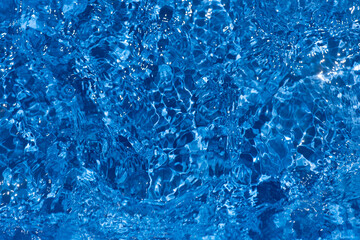 Blue water with ripples on the surface. Defocus blurred transparent blue colored clear calm water surface texture with splashes and bubbles. Water waves with shining pattern texture background.