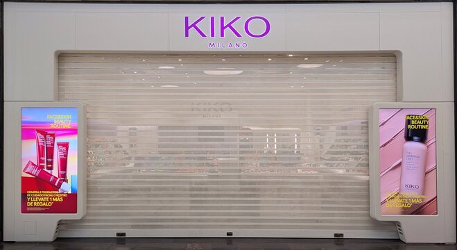 Fachada de tienda de perfumes Kiko Milano, con puerta cerrada por cortina plegable de metal, en centro comercial Islazul, Madrid, Espa&ntilde;a, 28 octubre 2025