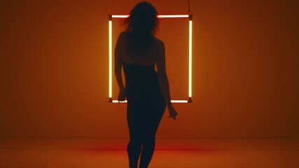Woman silhouette steps away from the camera, taking her place before the glowing neon square as she starts to dance - Powered by Adobe