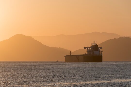 Silhouette of a cargo ship sailing in Santos city Bay, Brazil, during sunset.