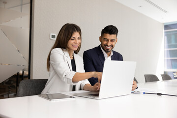Two multiethnic coworkers discussing online content on laptop
