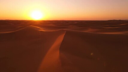 Majestic aerial drone shot flying low over vast desert sand dunes, creating abstract undulating patterns of light and shadow during a golden hour sunset overhead, travel, sand - Powered by Adobe