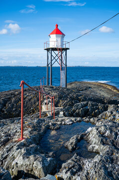 Kvalen fyr, a red and white lighthouse stands on rocky terrain by the sea, with a pathway leading to it, vertical shot, Haugesund, Norway