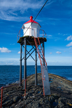 Kvalen fyr, red and white lighthouse stands on a rocky outcrop by the sea, with a clear blue sky above, Haugesund, Norway, vertical shot