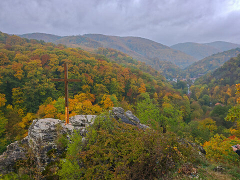 Wooden cross on the Moln&aacute;r Rock above Lillaf&uuml;red, Hungary, surrounded by colorful autumn forest and mountain peaks under dramatic clouds. Peaceful natural scene.