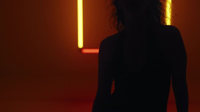 Close up of woman's feet as she walks toward the camera in a rhythmic catwalk style, black silhouette outlined against neon square