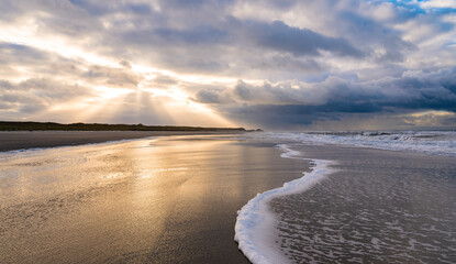 Idyllic beach panorama on the North Sea island of Norderney in the Wadden Sea National Park (Germany) in the atmospheric golden light of the autumn evening sun, reflected in the water and wave surf. 