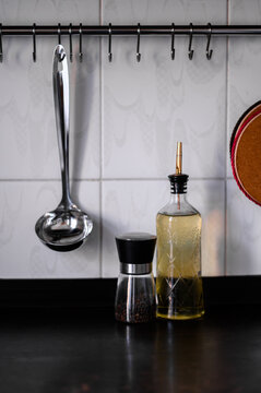 The ladle is hanging on a hook on the wall and there is a pepper pot and a bottle of oil next to it