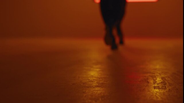 Close up of the heels of two women walking in catwalk style, steps synchronized against the background of the glowing neon square